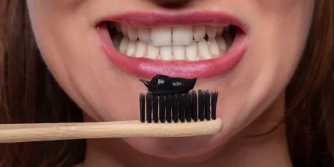 Cepillo de bambú con pasta dental de carbón activado frente a una sonrisa
